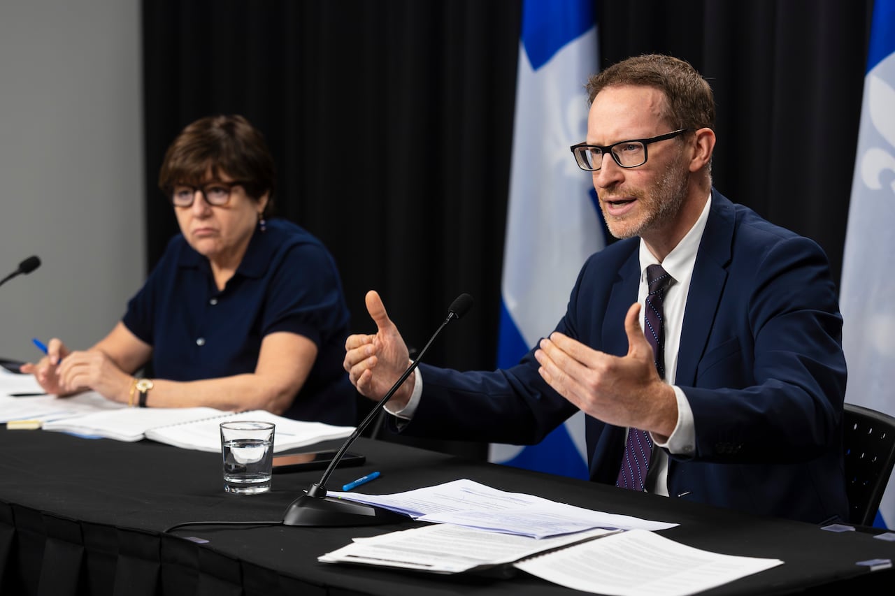 Two people sit behind a desk. 