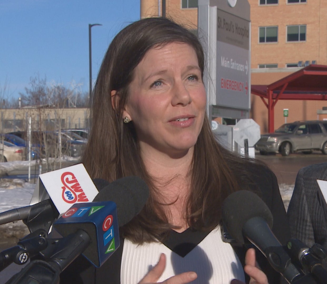 A woman speaks into microphones outside a hospital.