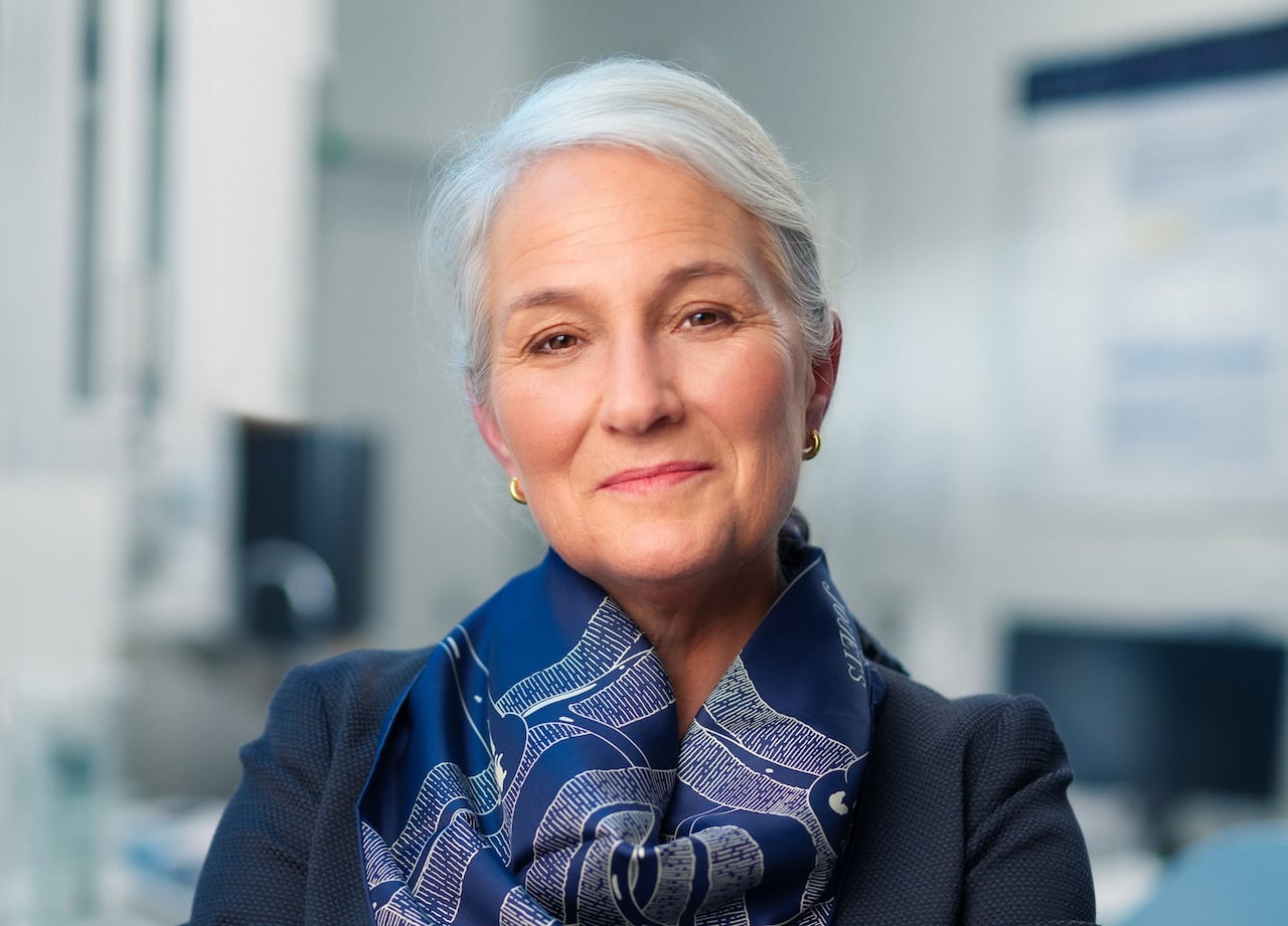 A white woman with a blue blazer and scarf smiles at the camera.