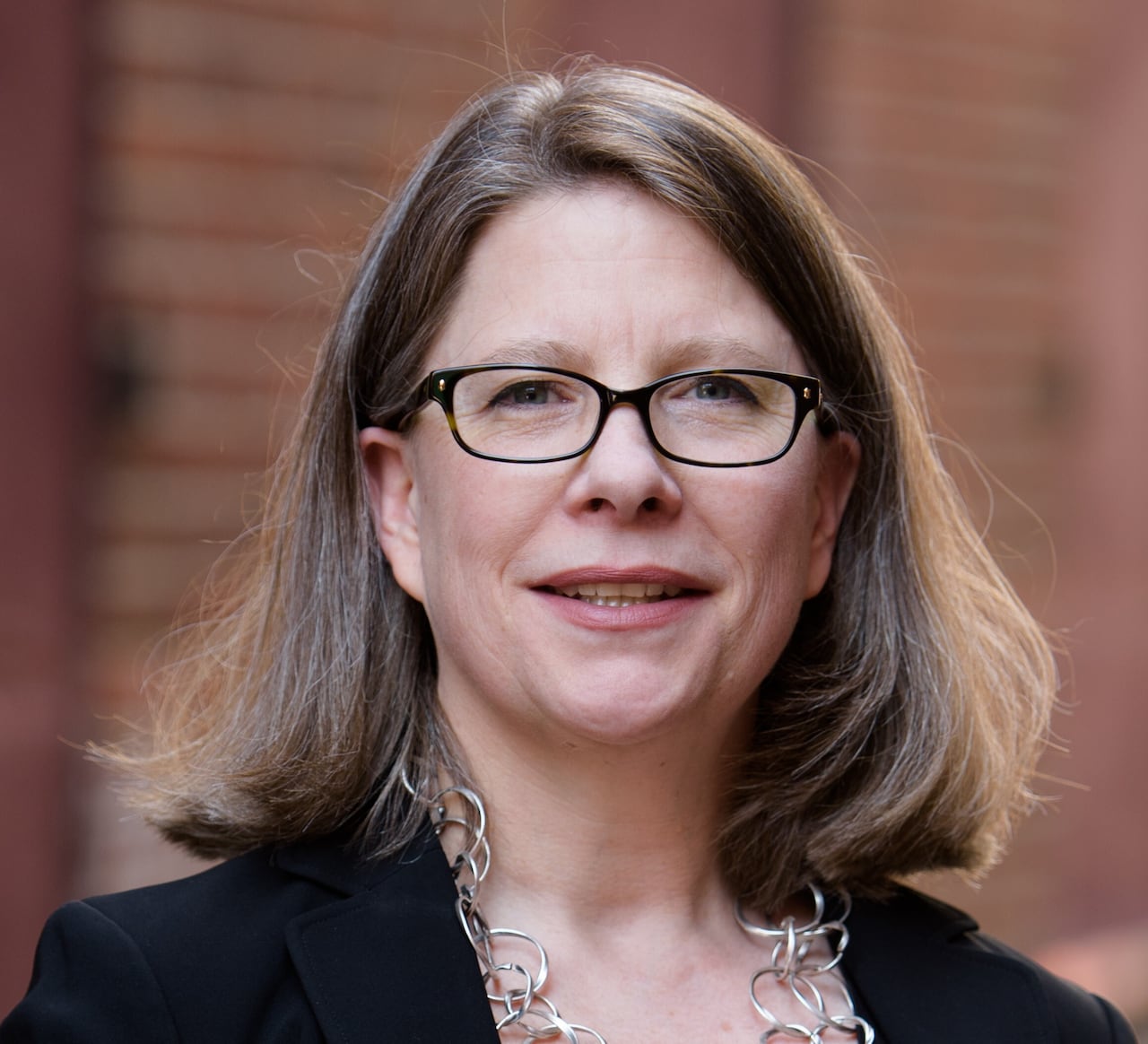 A white woman with shoulder-length brown hair and a black blouse looks at the camera.