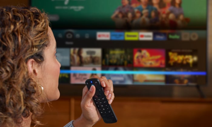 A person using the Alexa voice remote with a smart TV in the background.