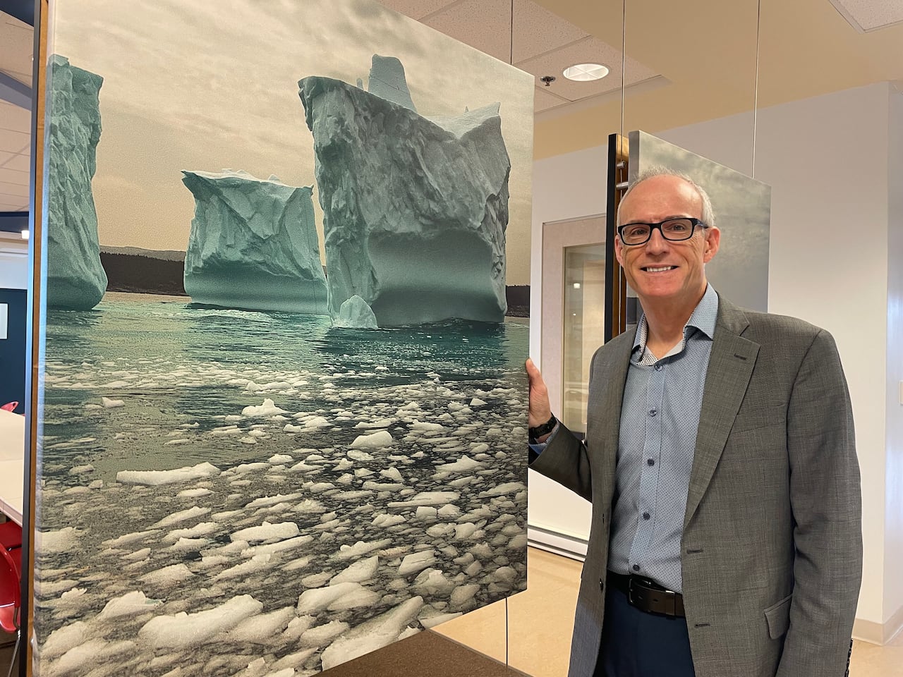 Man in a grey suit standing next to a picture of an iceberg