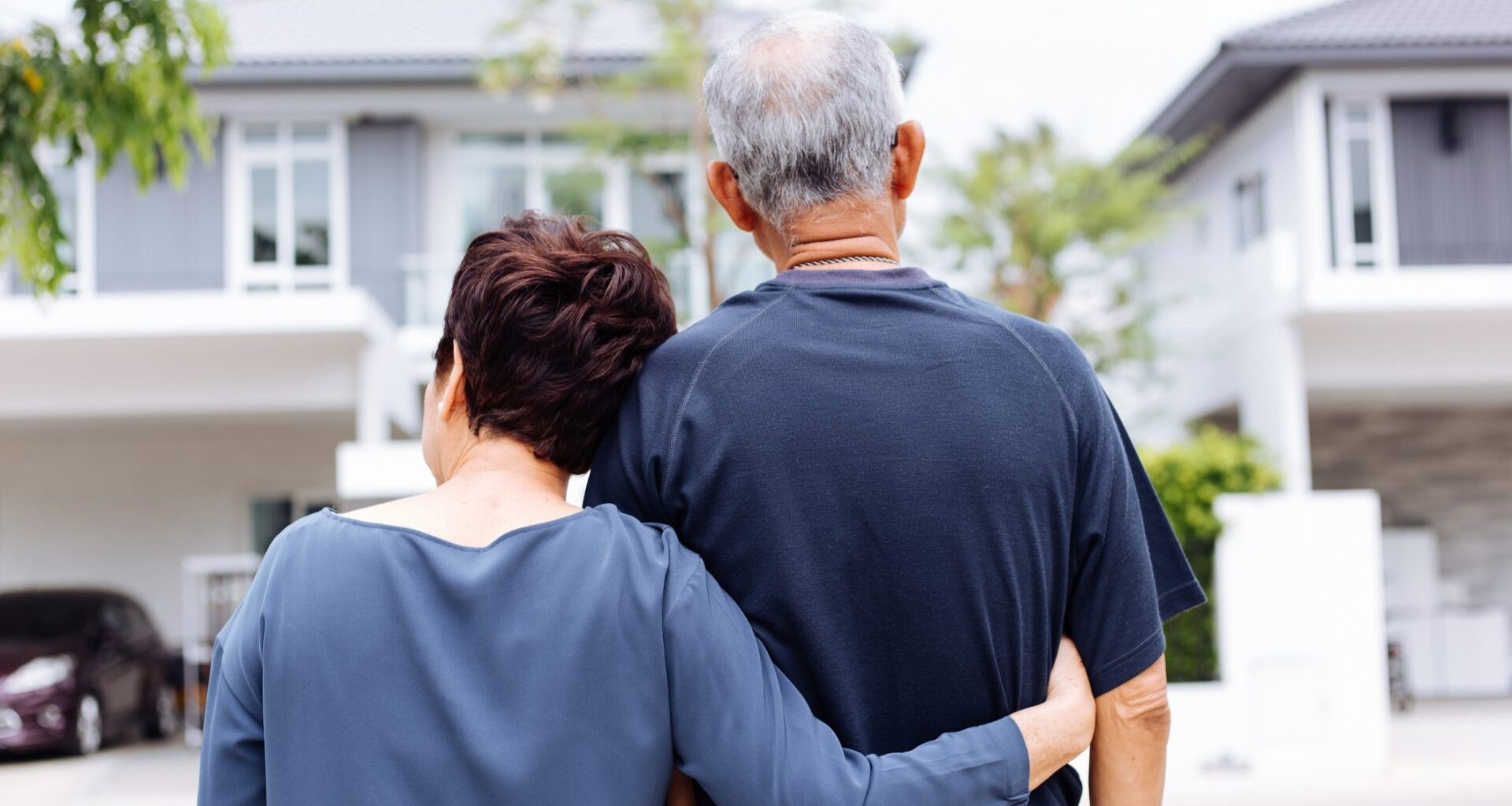 A senior couple embracing each other outside a home as they weigh downsizing their home during retirement.