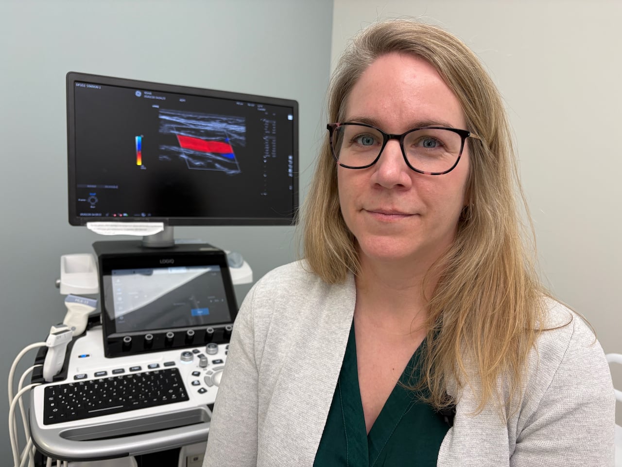 A woman sits beside an ultrasound machine.