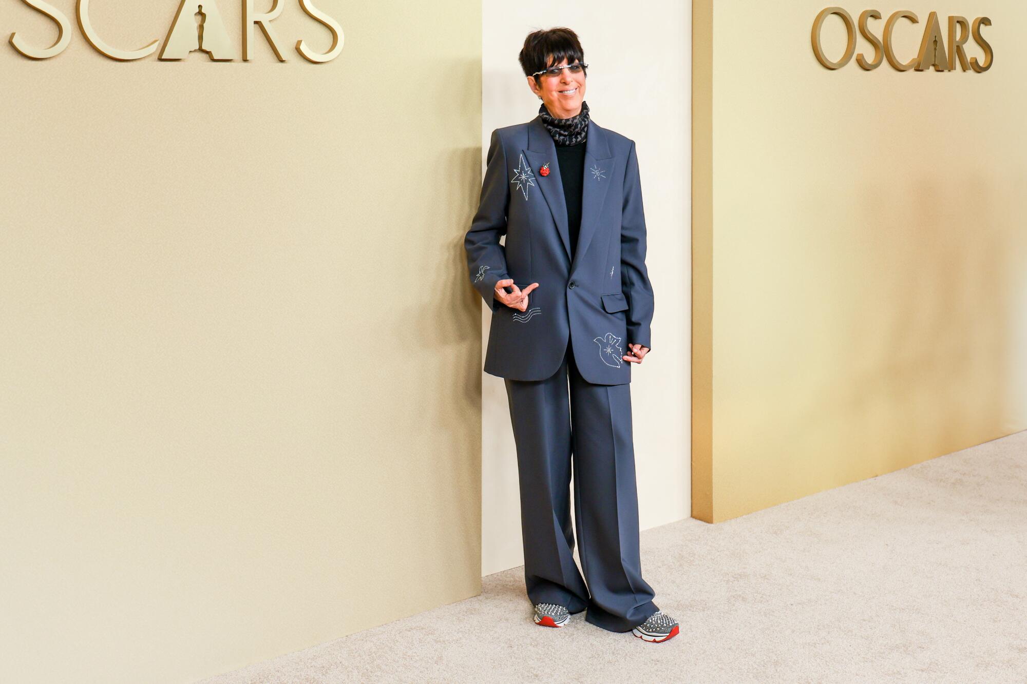 Diane Warren, wearing an oversized suit, poses on the beige carpet.