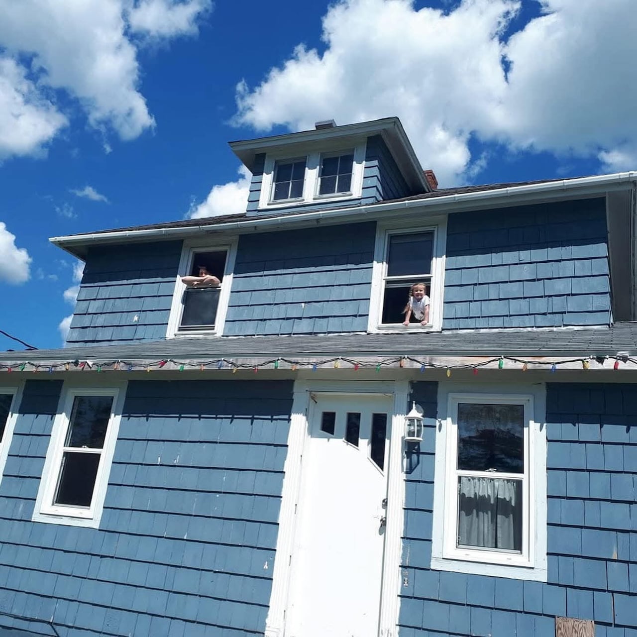 A blue house with two kids looking through the windows. 