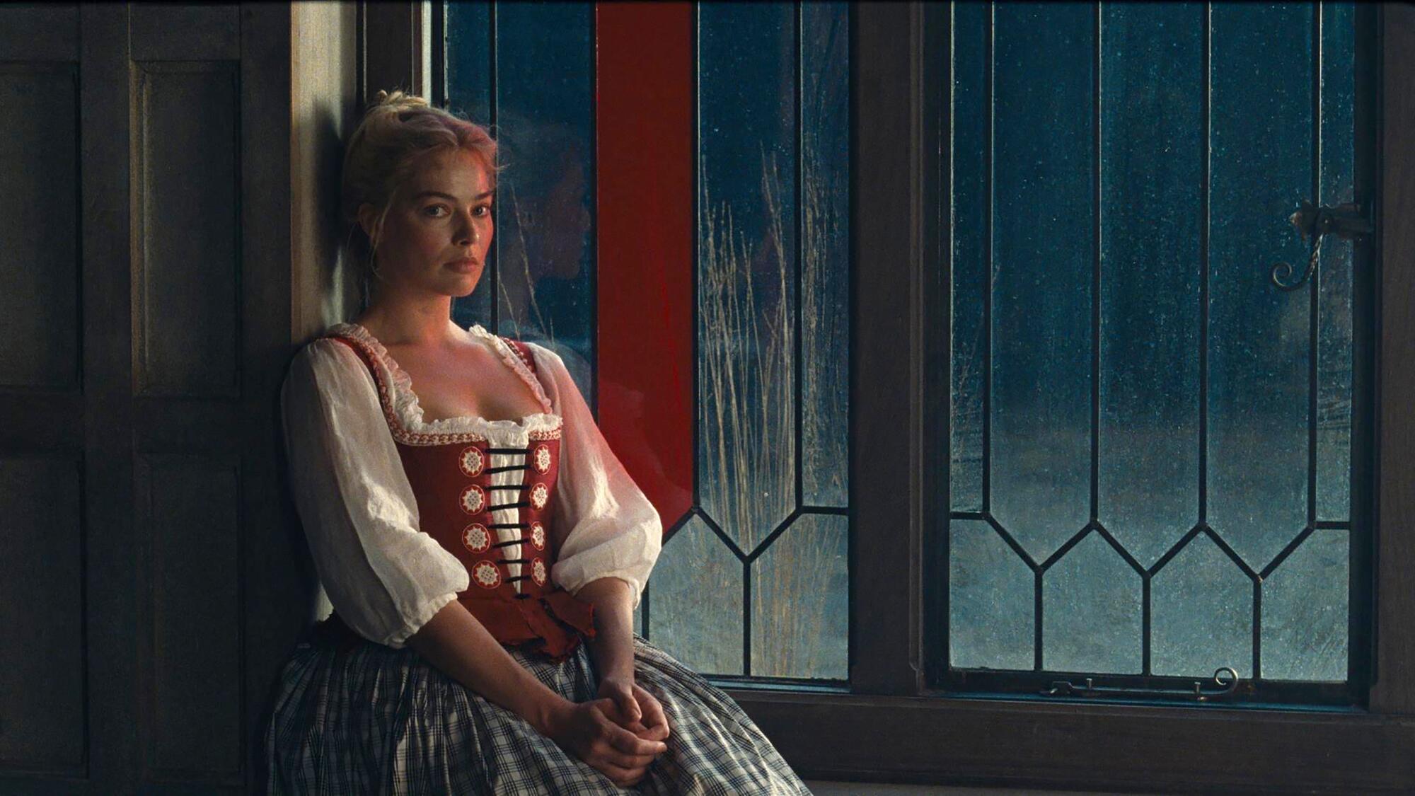 A woman in a dress sits in a window.