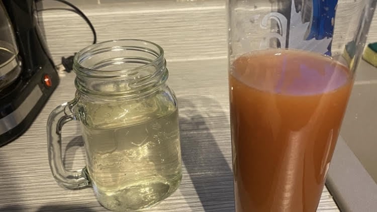 Two glasses of water for comparison. The untreated water on the right contains high manganese that causes rusty discoloration.