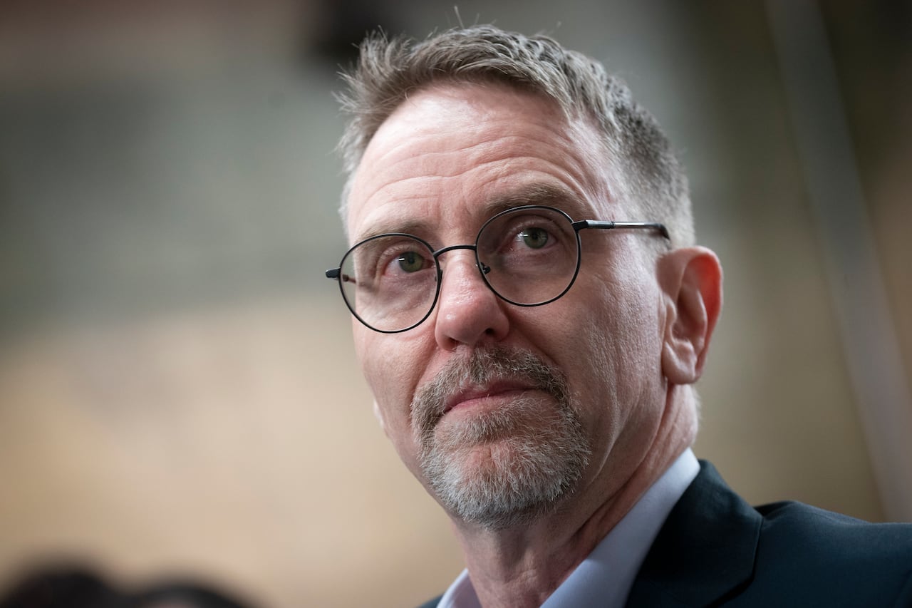 A man in glasses stares off into the distance.