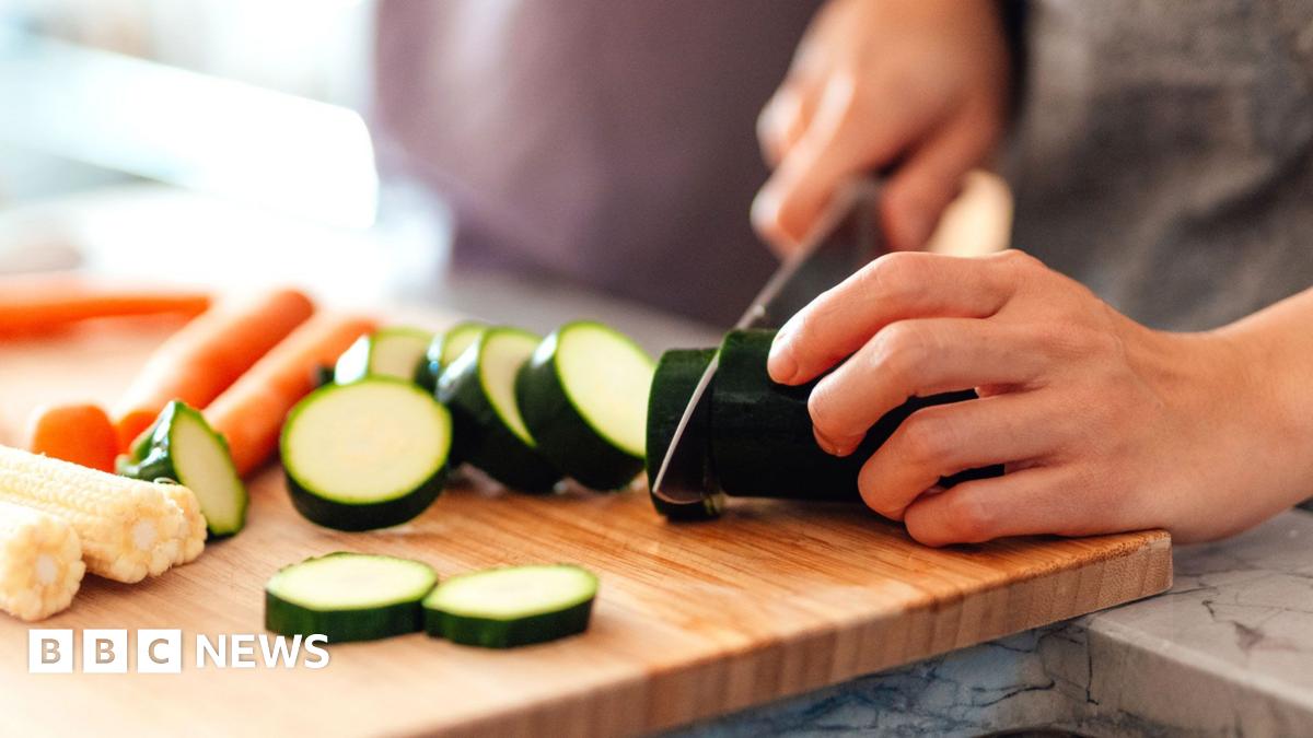 A person at home chops a courgette on a wooden chopping board