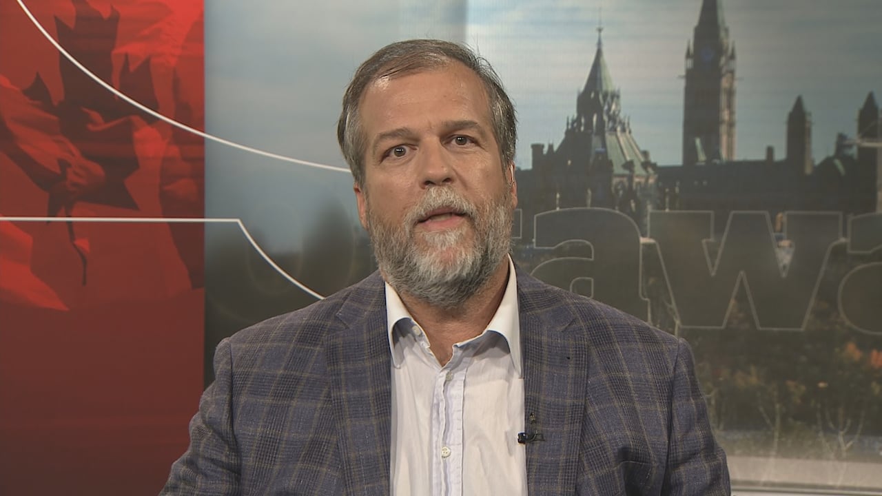 A man speaks against a TV backdrop.