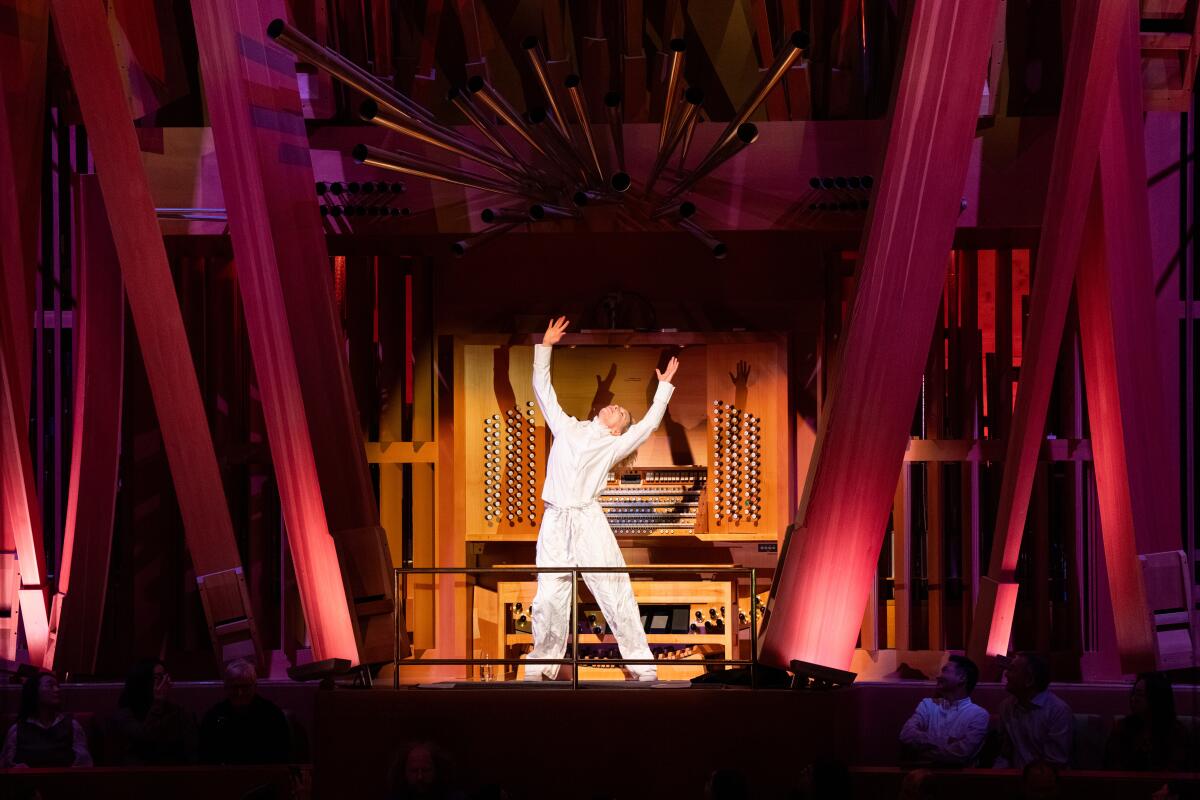 Cate Blanchett stands and holds up his arms in a white outfit on stage 