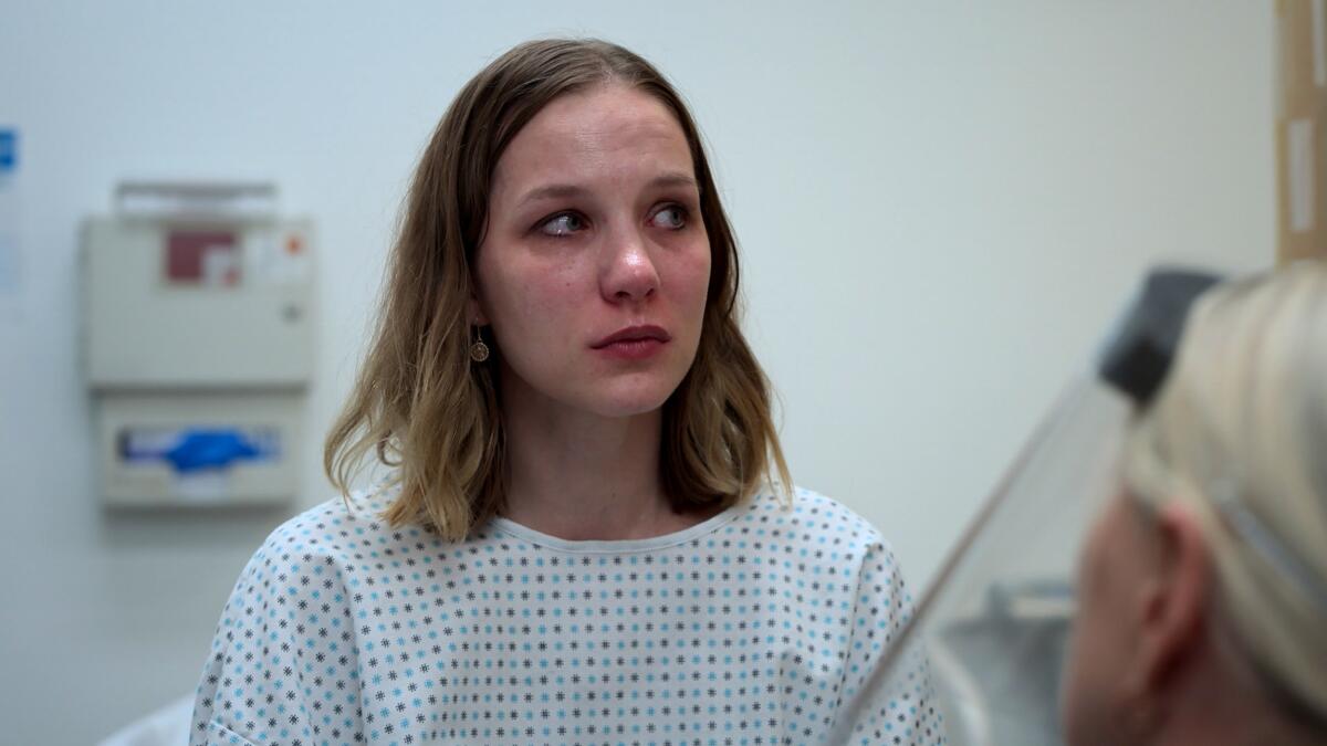 A young woman looking to her left in a hospital gown in a room