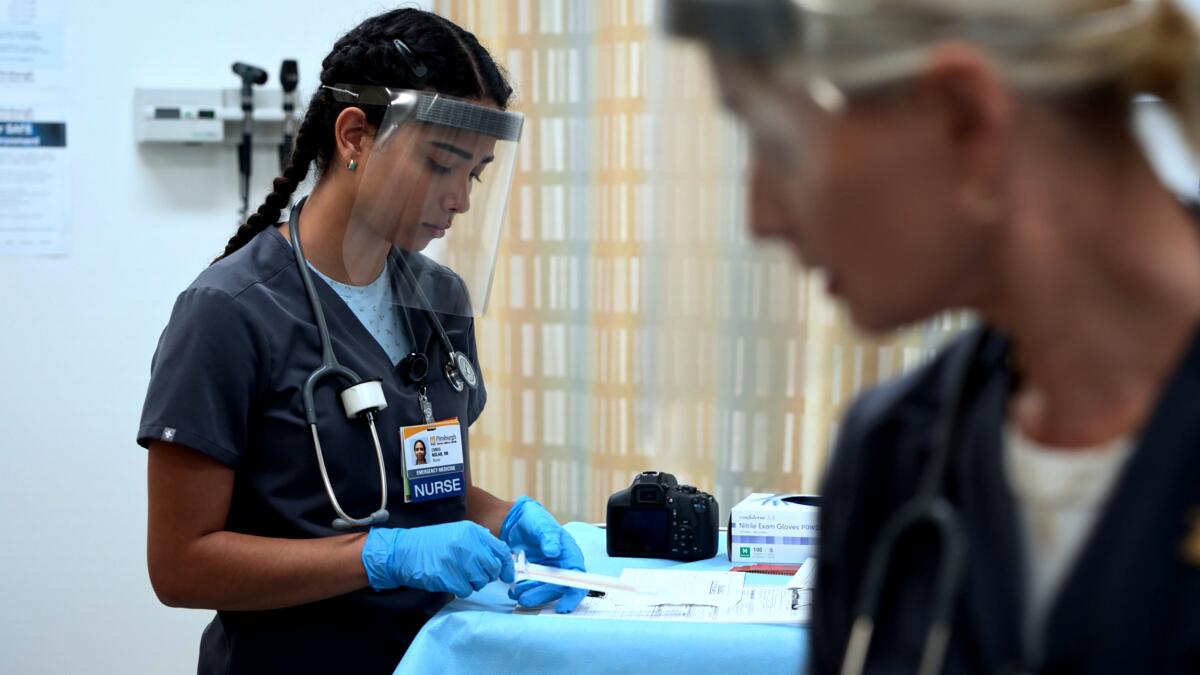 Two nurses, both wearing face shields, prepare for an exam