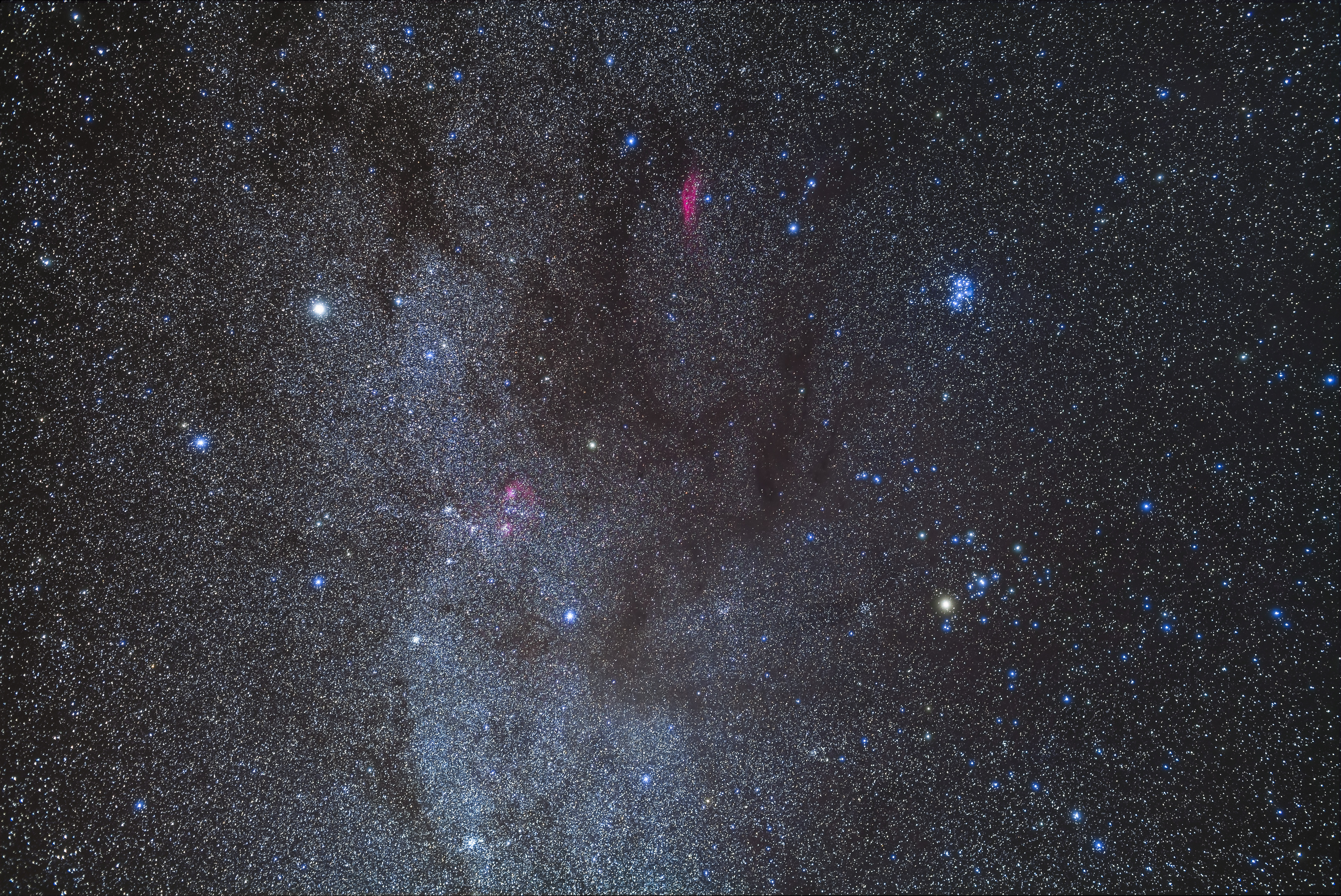 A picture of the night sky showing the glowing band of the Milky Way along with the blue-white stars of the Pleiades open star cluster.