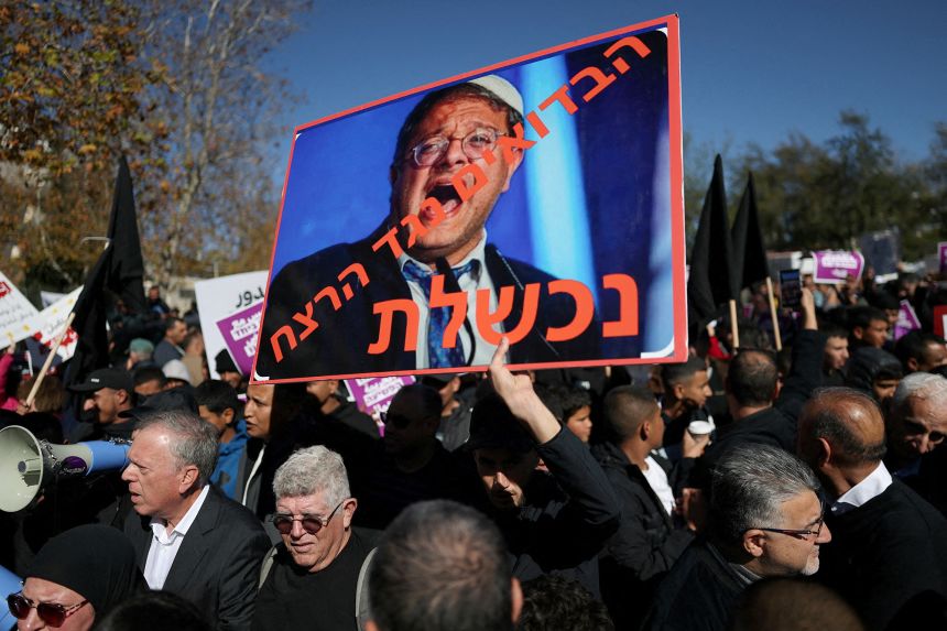 A demonstrator holds a sign with an image of Israeli National Security Minister Itamar Ben-Gvir and the words 