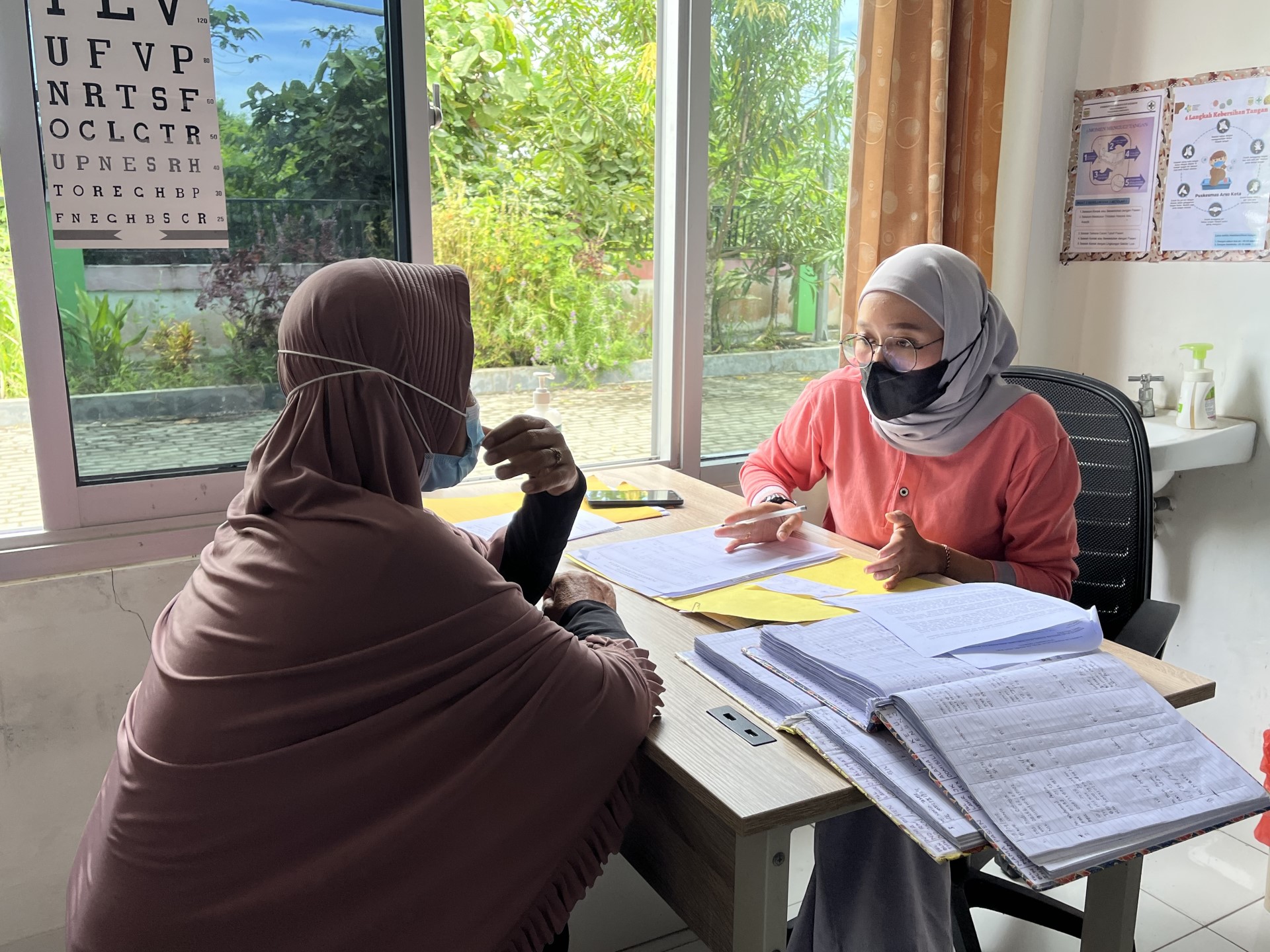 20260219 Antimalarial drug efficacy study 2 Two women in hijabs sitting across a table. One is a healthcare worker, the other one a patient.