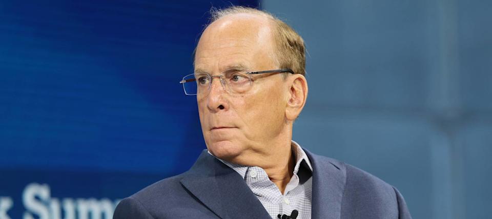 Larry Fink sits on stage in a blue suit and dress shirt, looking sharply over his right shoulder.
