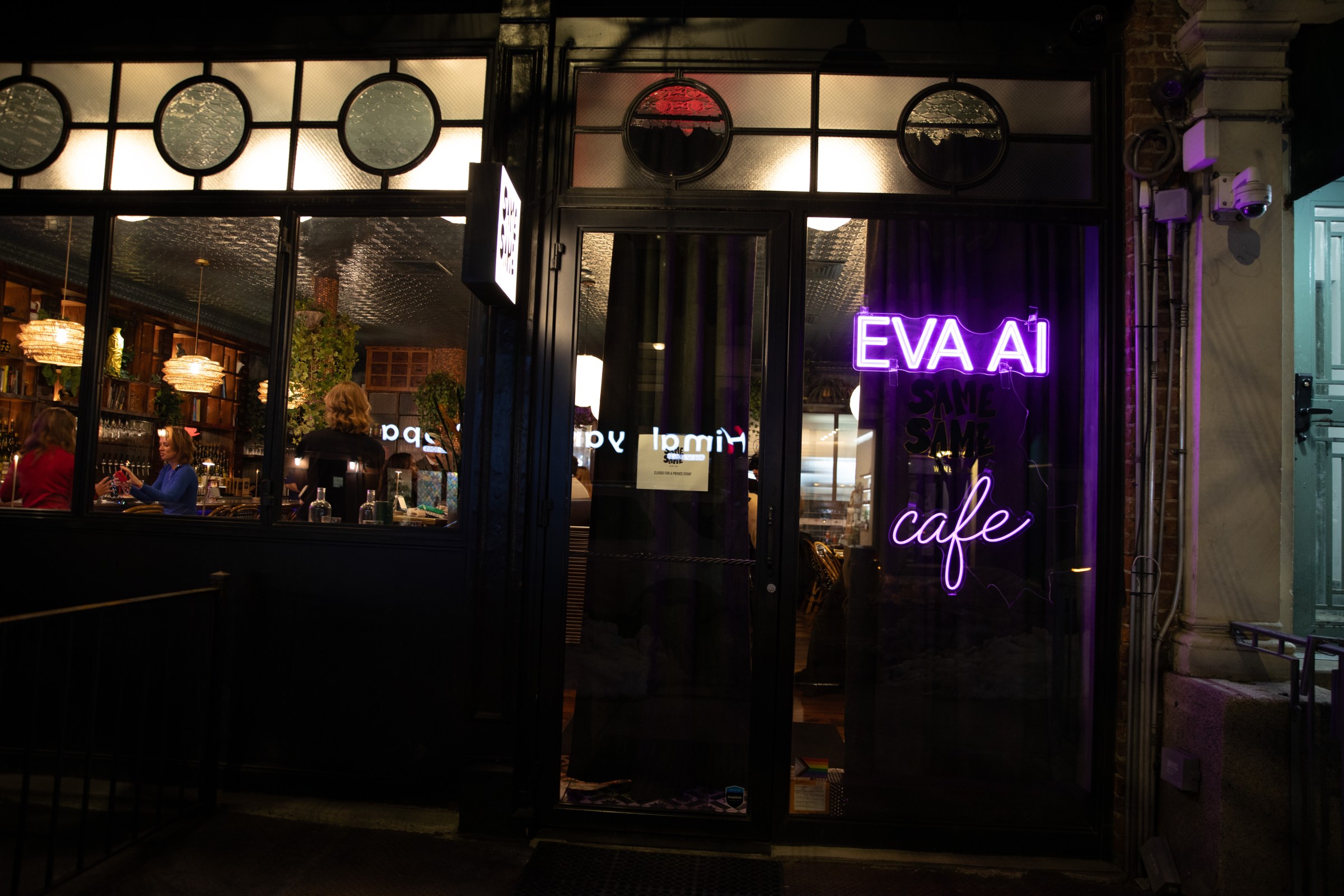 Outside view of a wine bar where you can see people through the window. In neon purple lights is the word EVA AI cafe.