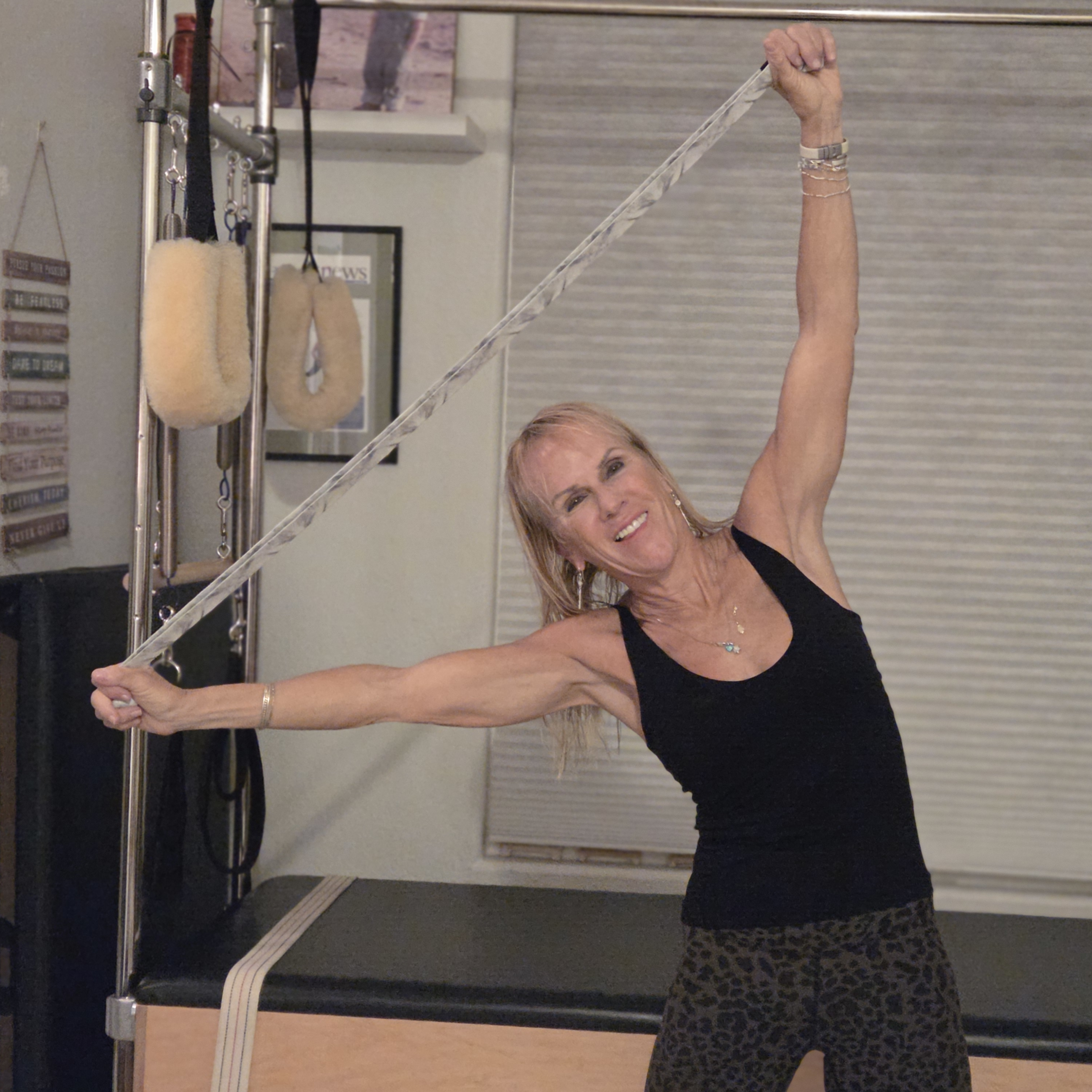 Woman stretching with yoga strap in front of a Pilates reformer bed