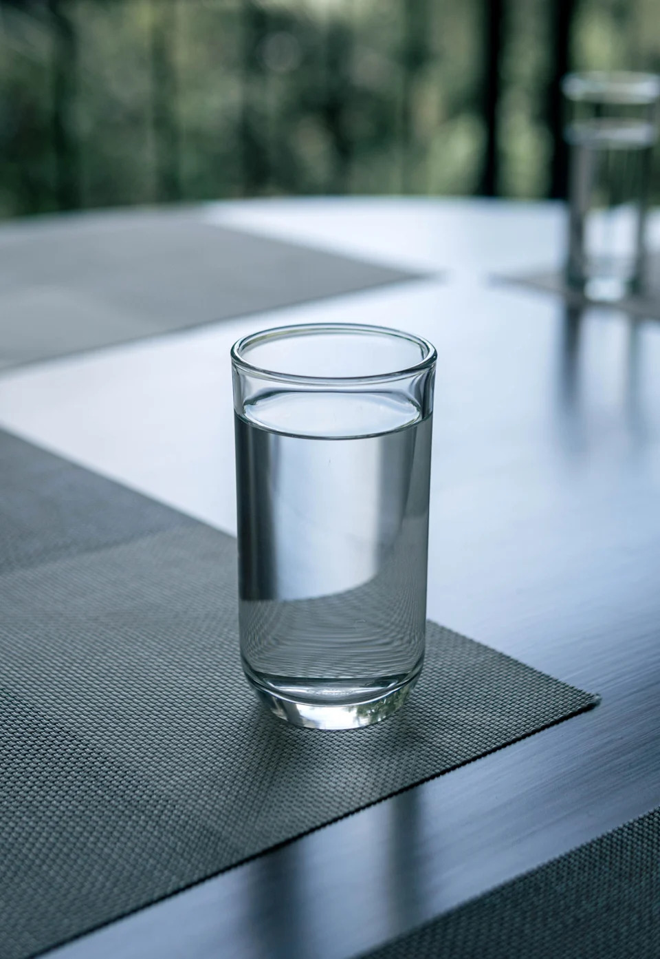 A clear glass of water sits on a table with a textured placemat, soft light coming through in the background