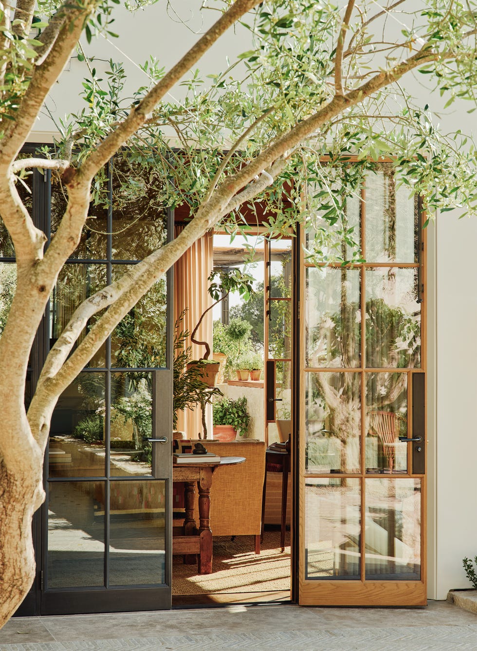 Open glass doors leading to a bright indoor space filled with plants and a rustic table.