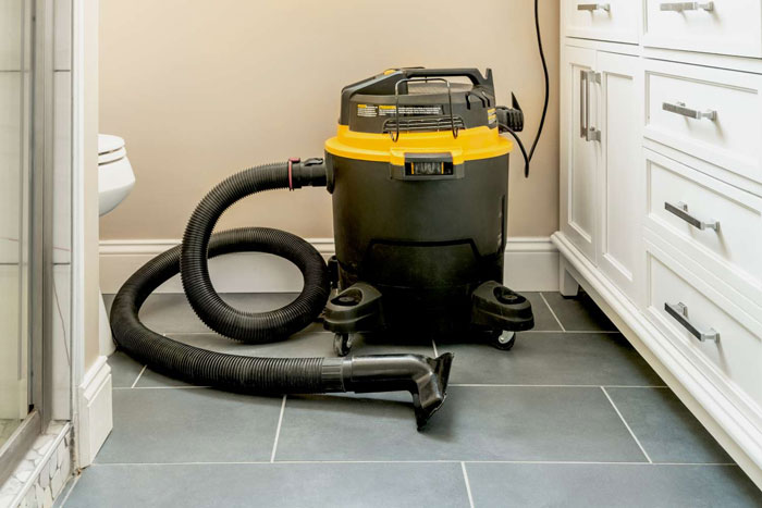 Wet dry vacuum cleaner with hose placed on tiled bathroom floor near white cabinetry, related to healthcare workers insights.