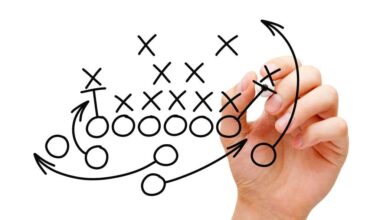 A hand draws football plays on a clear screen in black marker.