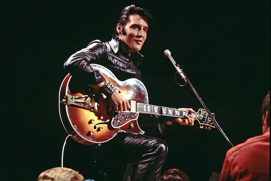 Elvis on stage performing behind a guitar