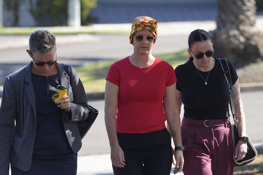 Three woman walk on street, middle woman wearing red top