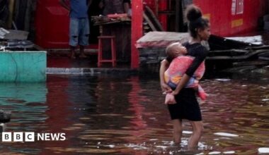 A girl carries an infant as she wades through water.