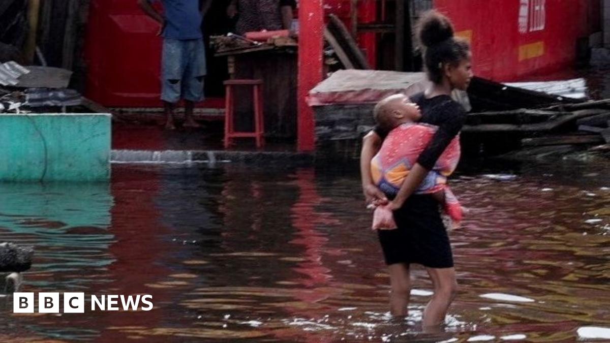 A girl carries an infant as she wades through water.