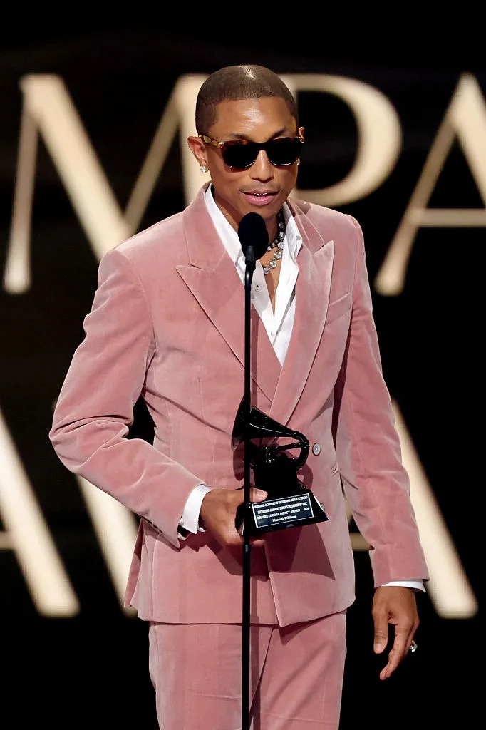 Person in a pink suit and sunglasses holding a Grammy award, speaking into a microphone on stage