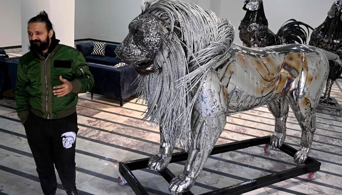 This photograph, taken on December 29, 2025, shows sculptor Ehtisham Jadoon standing next to his creation made from scrap metal, a lion with a mane of twisted steel, at his studio on the outskirts of Islamabad. — AFP