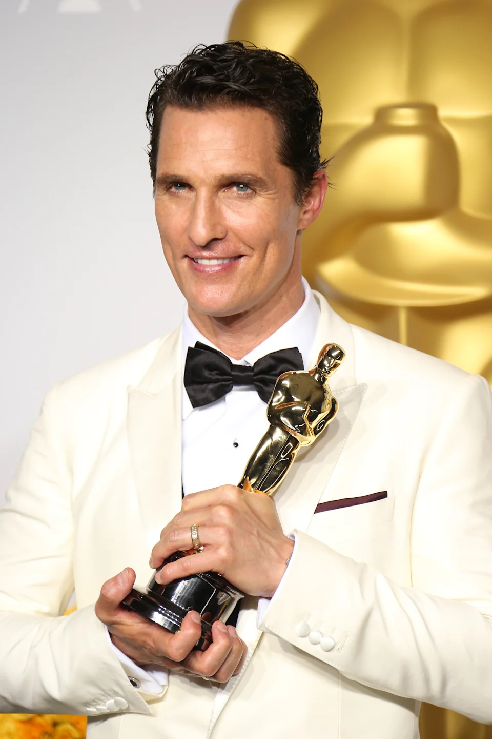 Person in a tuxedo holds an award statue, smiling at an event
