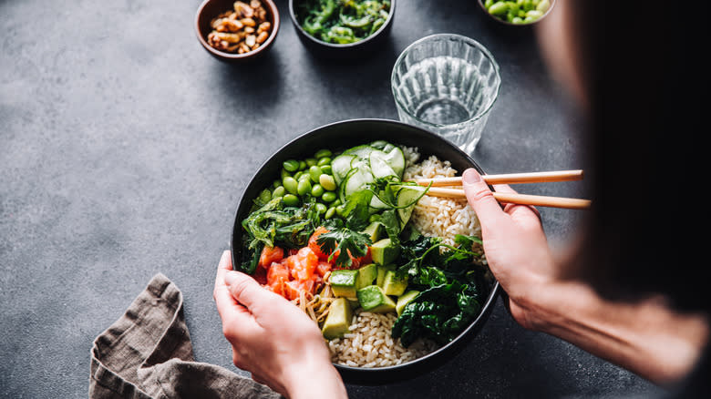 Hands holding bowl of brown rice topped with salmon and high-fiber vegetables