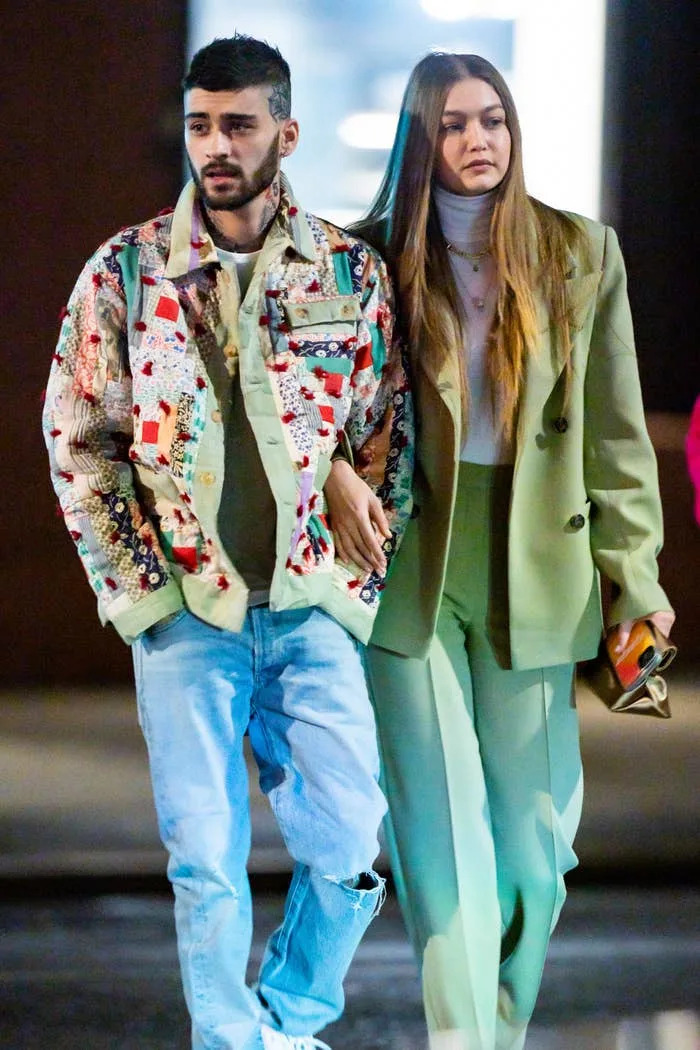 Two people walking; one in a patterned jacket and jeans, the other in a chic suit with long hair, both with a relaxed demeanor