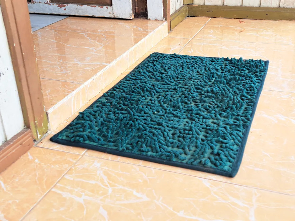 Textured doormat placed by a tiled step at a doorway, outside a home