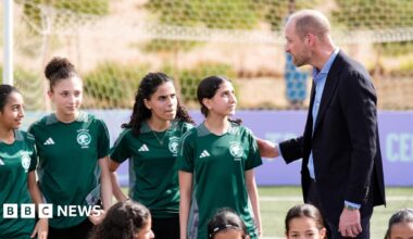 Prince William talks to a group of young girls in green football kits.