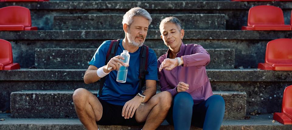 An older couple sit on the steps of a set of bleachers, resting after a work out.