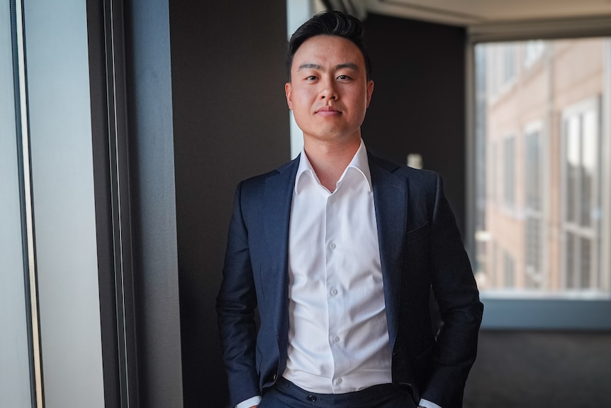 A portrait of a man in a business suit standing by a window, with hands in pockets.