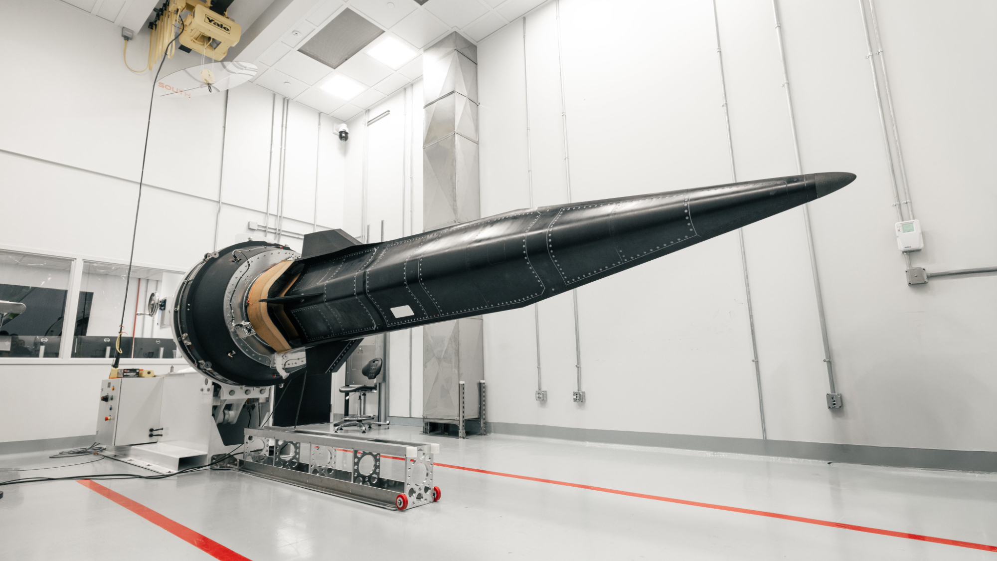 a black, knife-shaped spacecraft sits inside a white clean room