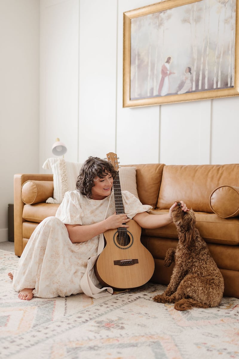 Angie Killian, composer of "Anytime, Anywhere," poses for a photo with her guitar and dog at her home in Salem, Utah, in 2024.