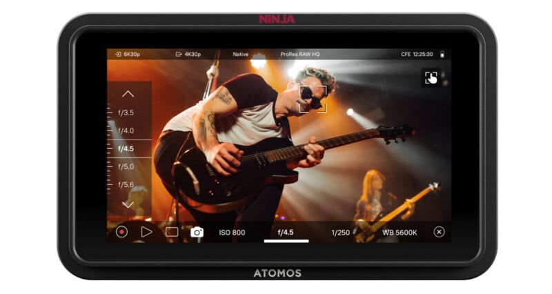 A camera monitor screen displays a live recording of a guitarist performing on stage, with camera settings such as ISO, shutter speed, and white balance visible on the sides of the display.