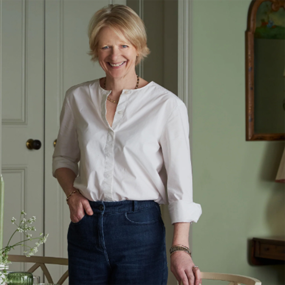 Birdie Fortescue in a white shirt and indigo jeans standing in a sage green room