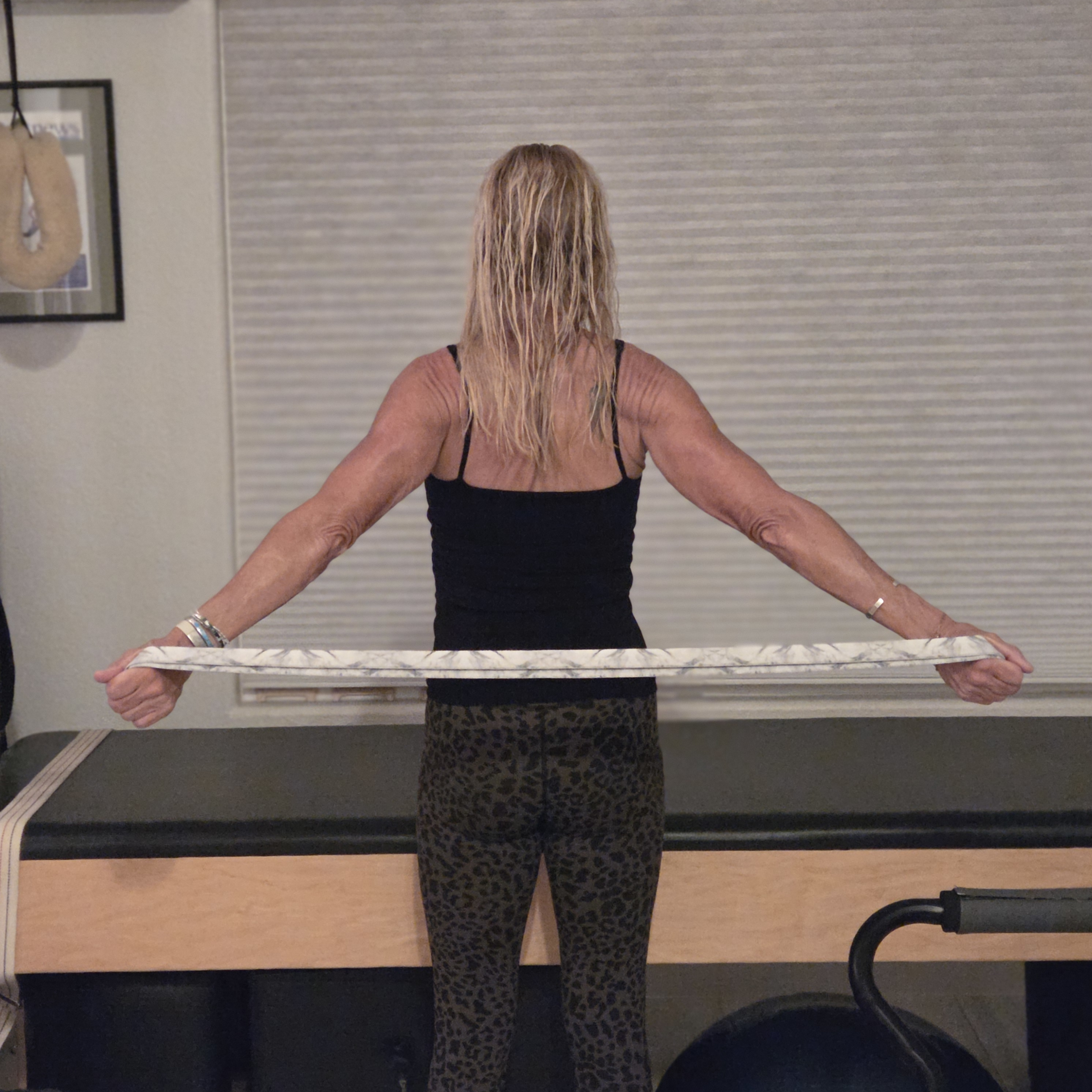 Woman stretching with yoga strap in front of a Pilates reformer bed