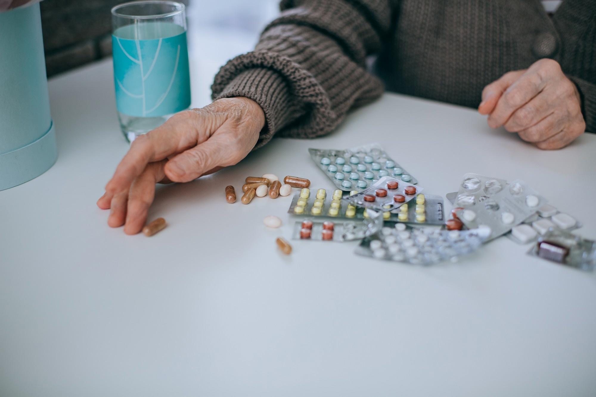 older adult hands next to lots of packets of tablet medication
