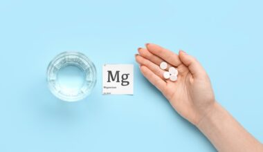 Female hand with magnesium pills and glass of water on blue background