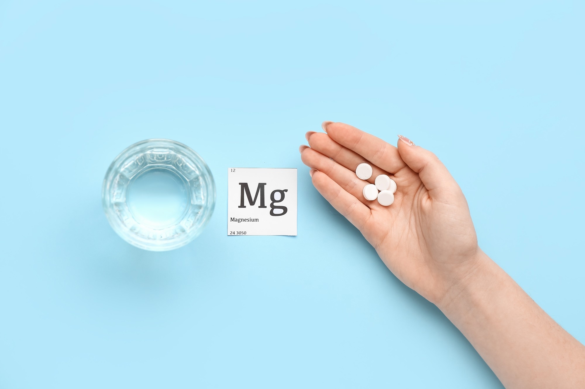 Female hand with magnesium pills and glass of water on blue background