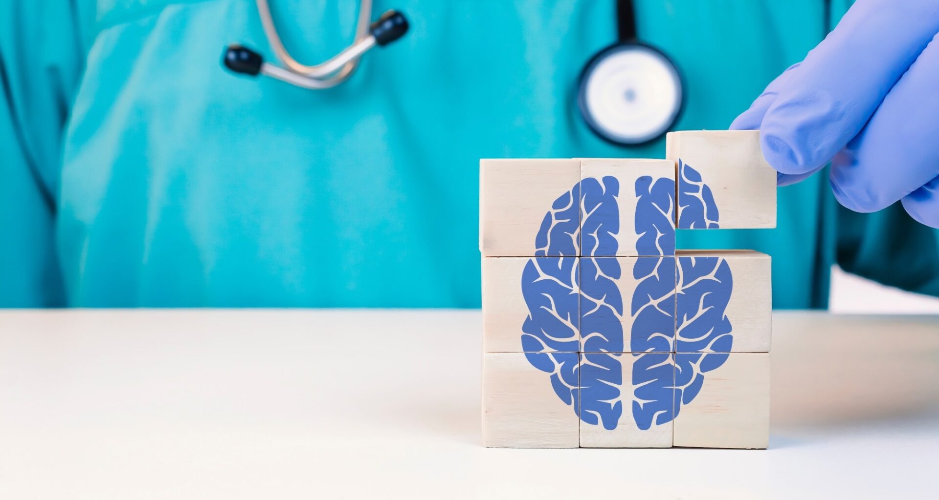 Doctor gloved hand stacking wooden blocks to form a square cube with a blue brain image on them